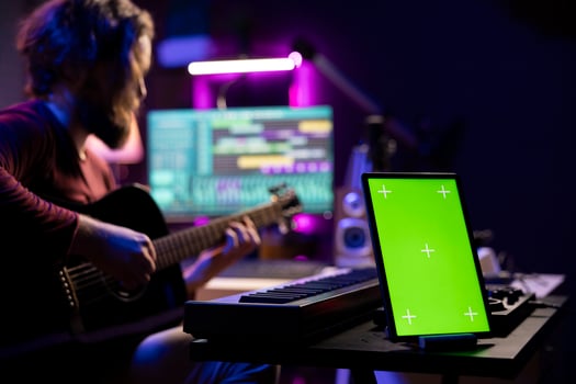 Audio engineer playing guitar and recording tunes on daw software, skilled artist learning to play new songs and strings accords. Music producer uses greenscreen on tablet, home studio. photo
