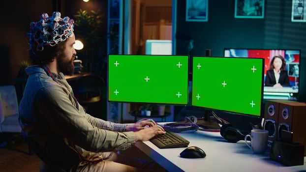 Engineer with EEG headset on programming brain transfer into computer virtual world on isolated screen monitors. Transhumanist using neuroscience to gain digital soul through chroma key PC, camera B photo
