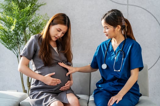 Smiling asian pregnant woman visiting doctor in prenatal clinic. Beautiful pregnant woman listening doctor advise on sofa. Closeup obstetrician consulting pregnant woman in hospital office. photo