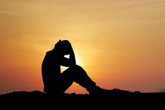 Silhouette of a Person Sitting at Sunset with Hands on Head, Contemplating and Reflecting in a Tranquil Outdoor Setting photo