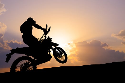 Silhouette of a Motorcyclist Performing a Wheelie Against a Vibrant Sunset Sky photo