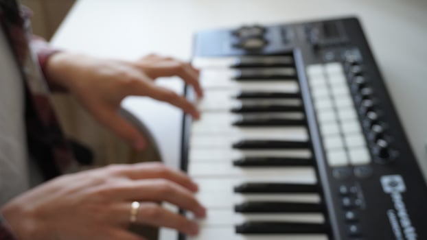 Recording music notes, playing electronic keyboard, midi keys in music sequencer. Hands and midi controller on the table, man composing music, blur photo