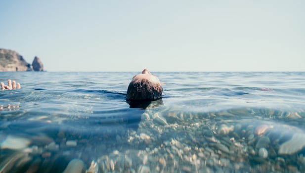 Woman swimming in sea at sunset, float on calm water back view. Concept of body image and fitness, enjoying a serene beach. Happy woman with perfect fit body enjoys sea beach photo