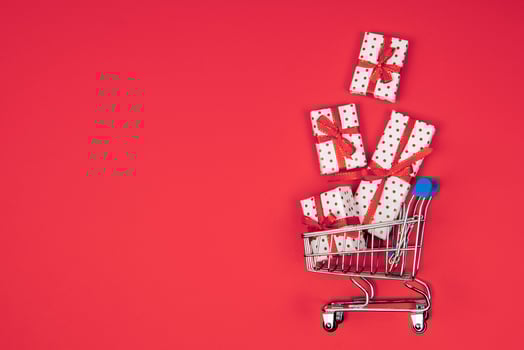 Flatlay shopping cart full of flying gifts on a red background with copy space. Holidays, discounts and christmas concept. photo