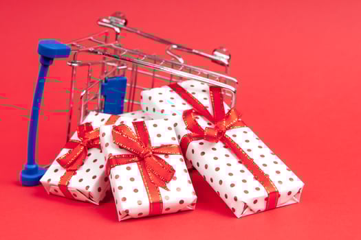 An overturned grocery cart full of gifts on a red background with copy space. Concept for christmas, holidays, discounts and shopping. photo