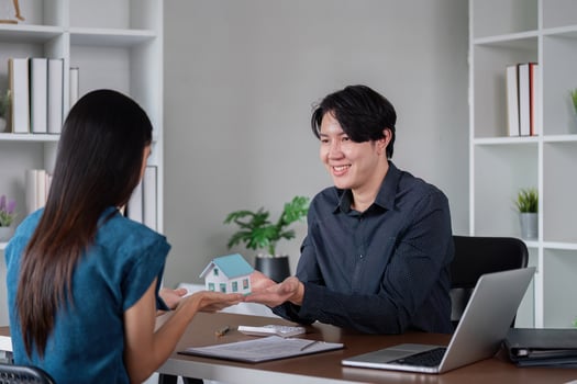 Real Estate Agent Showing Model House to Client in Modern Office Setting with Laptop and Documents photo