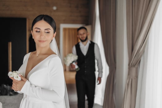 A bride and groom are standing in front of a curtain, with the bride holding a bouquet photo