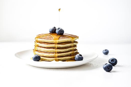 Stack of pancakes with blueberries and syrup on white background photo