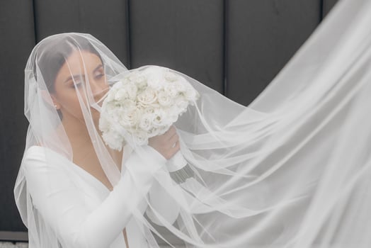A bride is wearing a veil and holding a bouquet of white flowers. The veil is white and covers her face, giving her a mysterious and elegant appearance photo