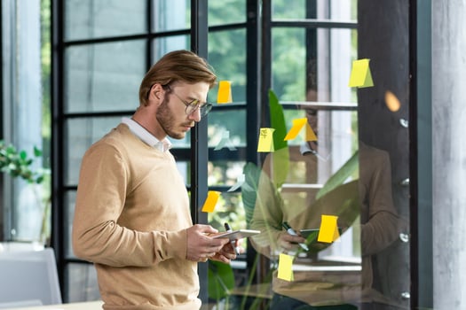 Portrait of a young programmer standing in the office near a glass transparent board and working with concentration on a tablet. Planning, developing, typing. photo