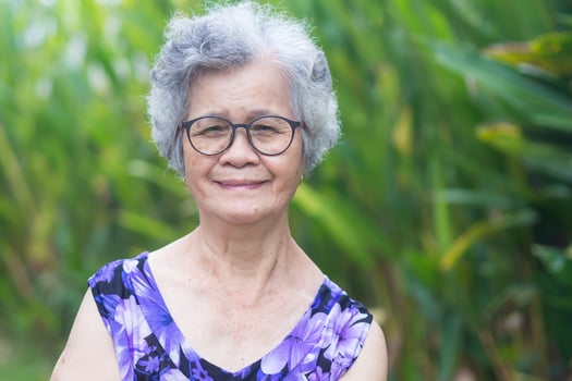 Portrait of a senior woman with short gray hair, wearing glasses, smiling and looking at the camera while standing in a garden. Aged people and relaxation concept photo