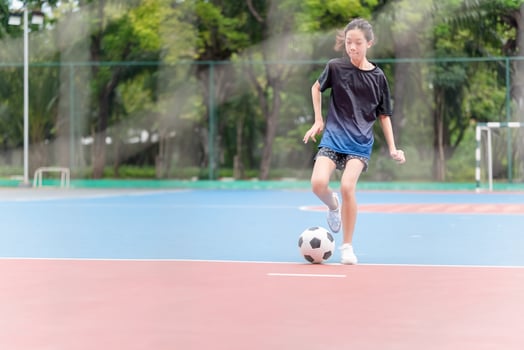 Asian child girl playing football in the urban outdoor futsal court photo