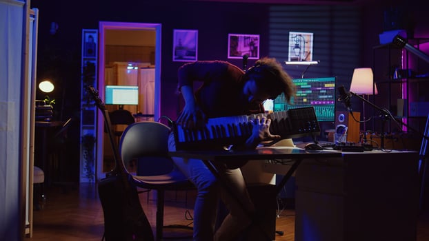 Energetic confident artist playing electronic piano in home studio, recording midi controller synthesizer notes to add audio effects. Cheerful sound engineer having fun with keyboard. Camera B. photo