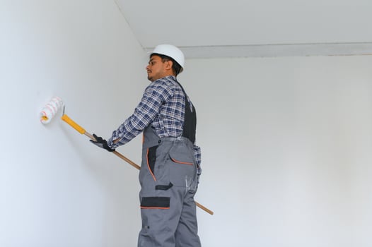 An Indian apartment repair worker paints a white wall with a roller. photo