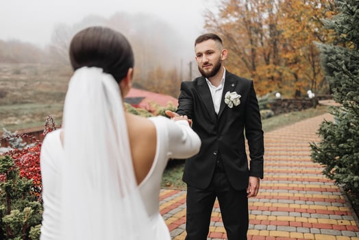 A bride and groom are standing on a brick walkway, the groom is holding the bride's hand photo