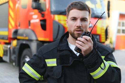 Firefighter in uniform using portable radio set near fire truck outdoors photo
