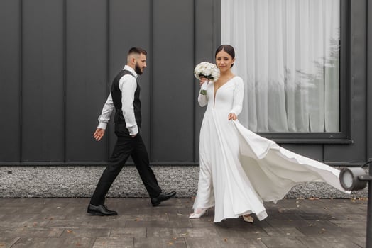 A bride and groom are walking down the street, the bride holding a bouquet. Scene is happy and celebratory, as the couple is getting married photo