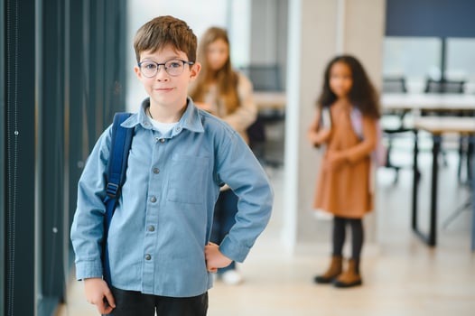 Happy cute clever boy in glasses with school bag and book in his hand photo