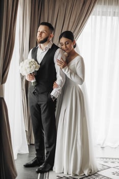 A bride and groom are standing in front of a curtain, with the bride holding a bouquet photo