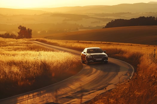 Prestige Full size sedan driving on winding countryside road with rolling hills and golden sunset light casting long shadows photo