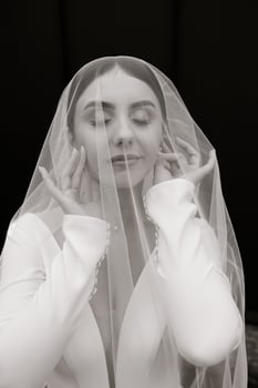 A woman is wearing a veil and looking at the camera. She is wearing a white dress and has her hands on her face photo