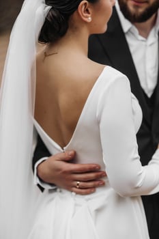 A bride and groom are posing for a picture. The bride is wearing a white dress and a veil, while the groom is wearing a black suit. The couple is embracing each other photo