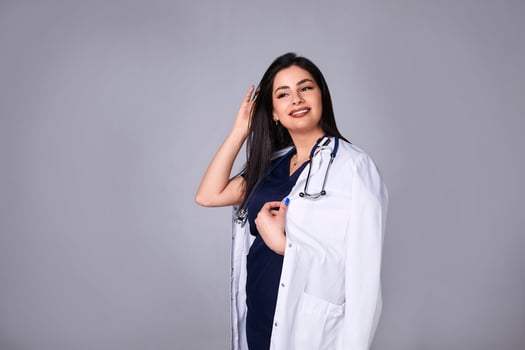 Portrait Brazilian beautiful female doctor in white coat with stethoscope, waist up. Medical student. Woman hospital worker looking at camera and smiling, studio, gray background photo