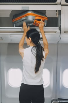 Young Female Tourist Storing Luggage in Overhead Compartment on Airplane During Travel photo
