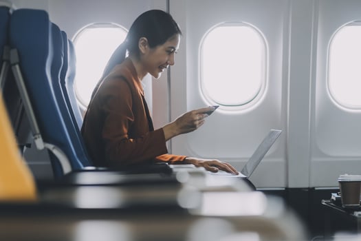 Asian female tourist checks notifications on smartphone while seated on airplane A businesswoman happily shares media from her phone, taking photos of the view from the window during a flight.