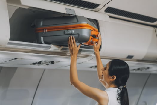 Young Female Tourist Storing Luggage in Overhead Compartment on Airplane During Travel photo
