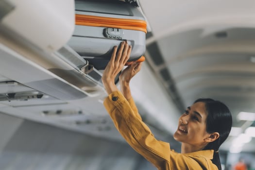 Young Female Tourist Storing Luggage in Overhead Compartment on Airplane During Travel photo