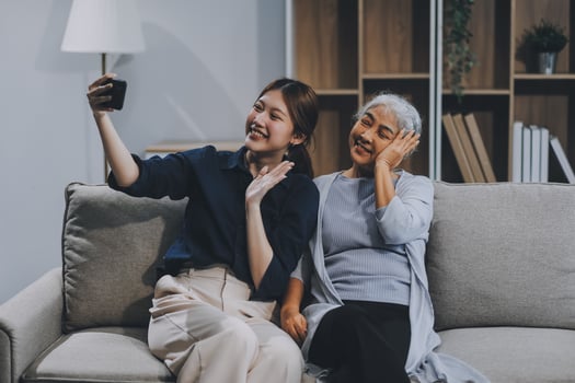 Cheerful mother and pretty teenager kid relaxing at cozy home, using mobile phone for Internet communication, resting on sofa with digital gadget, enjoying leisure, looking at camera photo