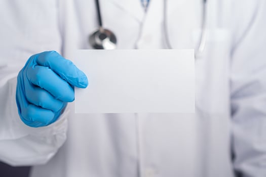 Hand of a doctor wearing protective gloves holding a white paper while standing in the hospital. Space for text. Medical and communication concept photo
