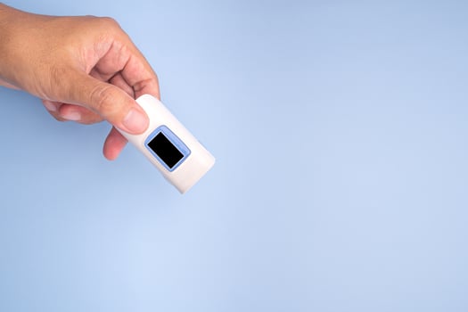 Hand holding of a pulse oximeter on a light blue background. Measurement of blood oxygen and pulse. Lung disease. Close-up photo. Space for text. Healthcare concept photo