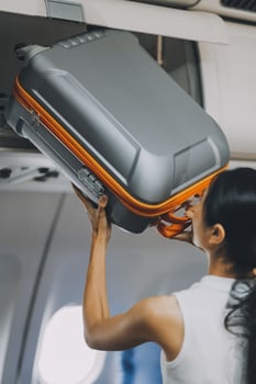 Young Female Tourist Storing Luggage in Overhead Compartment on Airplane During Travel photo