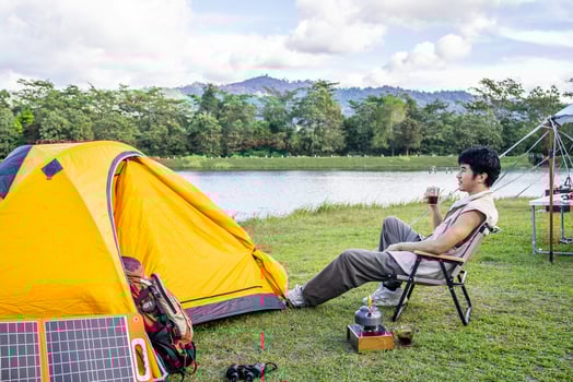 Young Asian traveling man relax and enjoy outdoor lifestyle camping in forest mountain on summer holiday travel vacation. Attractive male drinking coffee while enjoys drink among green trees photo