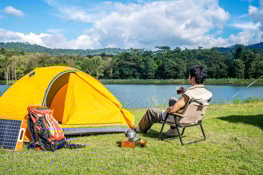 Young Asian traveling man relax and enjoy outdoor lifestyle camping in forest mountain on summer holiday travel vacation. Attractive male drinking coffee while enjoys drink among green trees photo