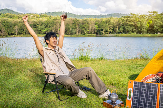 Young Asian traveling man relax and enjoy outdoor lifestyle camping in forest mountain on summer holiday. Attractive male drinking coffee and raise your hands refreshingly in the midst of nature photo