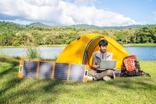 Young travel man relax and enjoy camping . Hand male plug in portable solar panel charging laptop computer by multipurpose cable, Clean energy for using in camping or at home when NO electricity photo