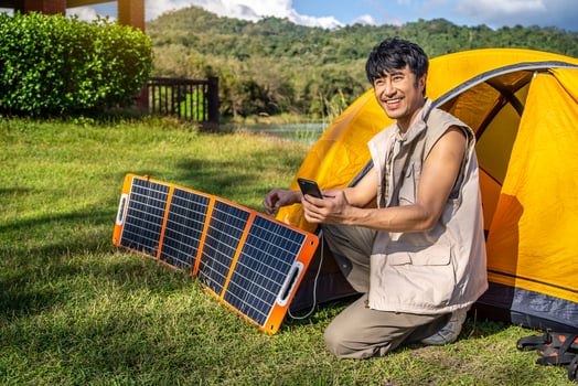 Young travel man relax and enjoy camping . Hand male plug in portable solar panel charging smartphone by multipurpose cable, Clean energy for using in camping or at home when no electricity photo