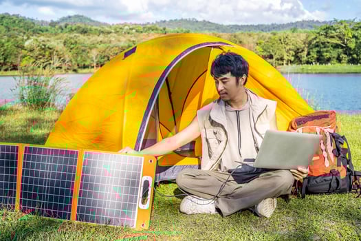 Young travel man relax and enjoy camping . Hand male plug in portable solar panel charging laptop computer by multipurpose cable, Clean energy for using in camping or at home when NO electricity photo