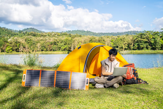 Young travel man relax and enjoy camping . Hand male plug in portable solar panel charging laptop computer by multipurpose cable, Clean energy for using in camping or at home when NO electricity photo