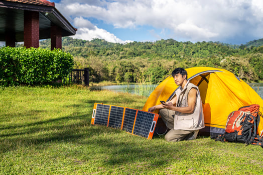 Young travel man relax and enjoy camping . Hand male plug in portable solar panel charging smartphone by multipurpose cable, Clean energy for using in camping or at home when no electricity photo