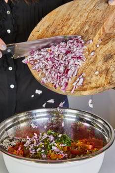 Close-up of hands using a knife to throw fresh onions from a wooden cutting board into a pan in the kitchen photo