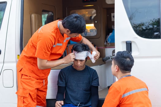 A man with a bandaged head is being helped by two other men in orange. The scene is serious and focused on the injured man photo