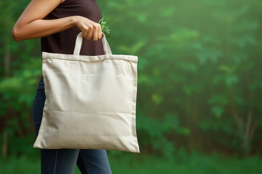 a woman holding open the front of a beige canvas bag to collect, photo