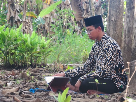 An Asian Muslim man is sitting and reading the Quran. The peace in the middle of forest makes it an energetic atmosphere of faith, traditional vibes photo