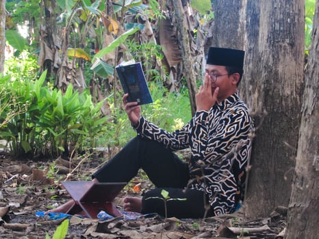 An Asian Muslim man is sitting and reading the Quran. The peace in the middle of forest makes it an energetic atmosphere of faith, traditional vibes photo