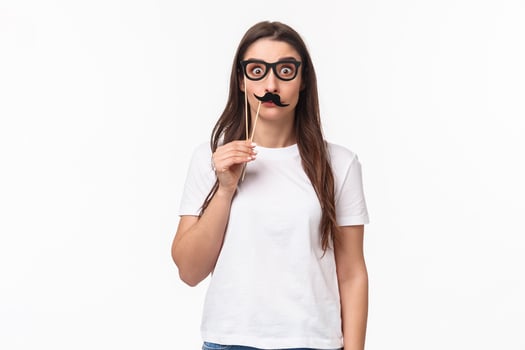 Entertainment, fun and holidays concept. Portrait of funny, playful and carefree girl holding carnaval mask sticks, fancy moustache and glasses, staring camera with popped eyes, white background photo