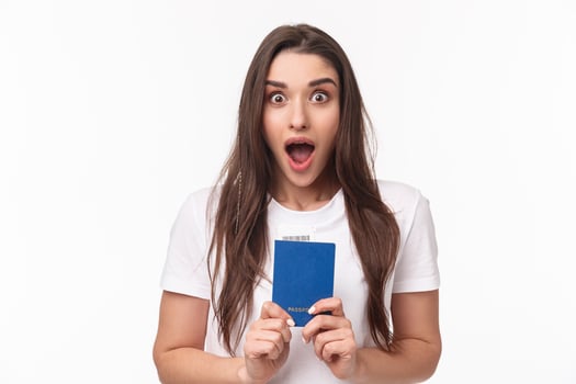 Travelling, holidays, summer concept. Close-up portrait of impressed, shocked young woman holding passport, drop jaw and staring astonished at camera, ready to travel, moving abroad photo